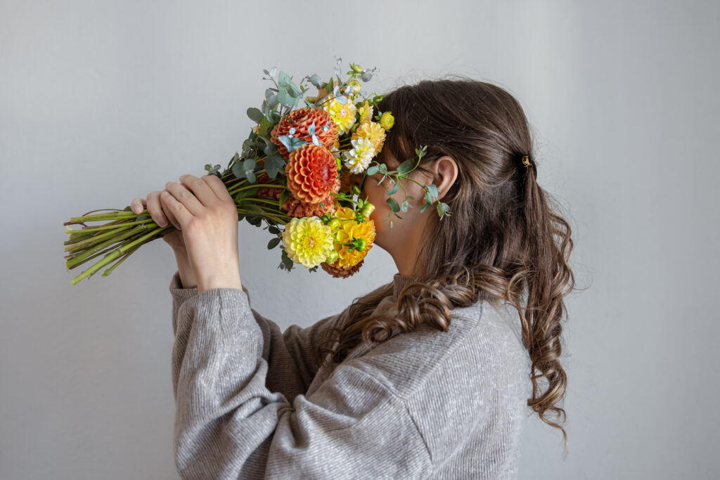 Young woman with a bouquet of fresh chrysanthemums on a gray background.